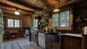 A rustic cabin kitchen with wooden walls, a central island with a sink, and hanging pots. - Rustic Historical Cabin near Wineries & Gold Mines (Dahlonega)