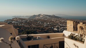 Vista elevada sobre un pueblo costero, con una imagen despejada del mar y montañas distantes.