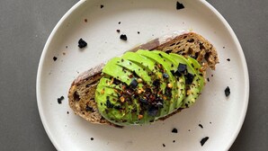 Dos tostadas con aguacate sobre una superficie oscura.