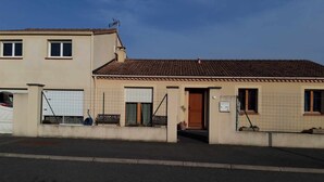 A two-story building with a tiled roof, a gated entrance, and a visible door. - Maison à Louer Août 2024, Quartier Calme, Idéal Pour les Familles (Briatexte)