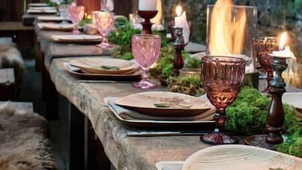 Un ambiente rústico para comer, con una mesa de piedra, velas y follaje.