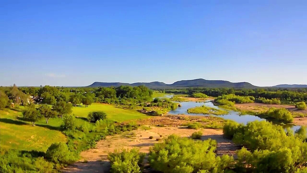 Paesaggio con un fiume, vegetazione e colline lontane.