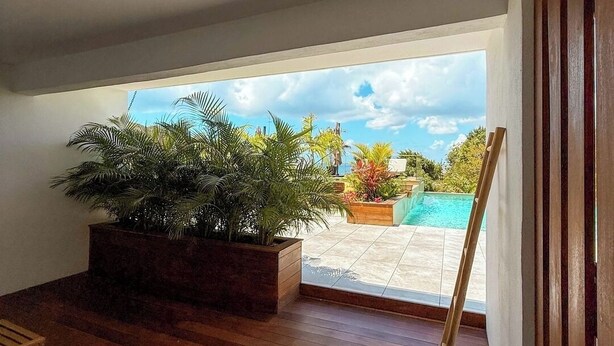 A room with wooden flooring, a large window, and a view of a swimming pool and garden. - Studio with direct access to the pool | Villa 5 (Pigeon-Pea Hill)