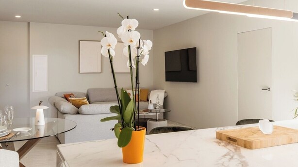 Una cocina moderna con encimera de mármol, tabla de cortar de madera y una orquídea en maceta.