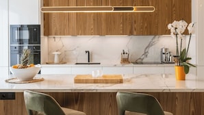 Una cocina moderna con armarios de madera, encimera de mármol, horno empotrado y una isla central con taburetes de bar.