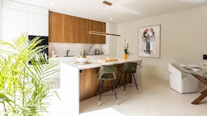 Una cocina moderna con una isla central, taburetes de bar y un comedor con una mesa para dos.