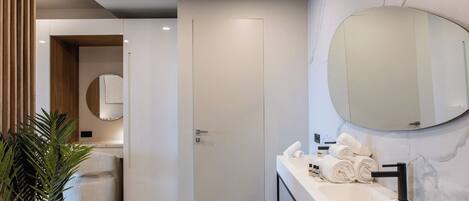 A modern bathroom with a long vanity, a large mirror, and a potted plant.