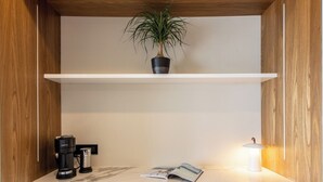 Um espaço de trabalho compacto com cafeteira, luminária e planta sobre uma estante branca.