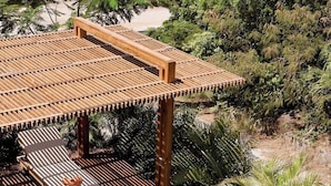 Area piscina con solarium in legno e lettini, circondata da vegetazione tropicale.