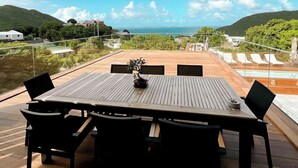 A wooden deck with a table and chairs, overlooking a body of water and a distant coastline. - 2 rooms ocean view and jacuzzi | Villa 8 (Pigeon-Pea Hill)