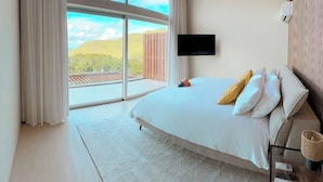 A bedroom with a large bed, a flat-screen TV, and a view of a hilly landscape through a large window. - 2 rooms ocean view and jacuzzi | Villa 8 (Pigeon-Pea Hill)