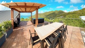 A wooden deck with a table and chairs, a barbecue grill, and a hot tub, overlooking a mountainous landscape. - 2 rooms ocean view and jacuzzi | Villa 8 (Pigeon-Pea Hill)