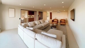 Un salon spacieux avec un grand canapé en forme de L, une table basse et un téléviseur fixé au mur.