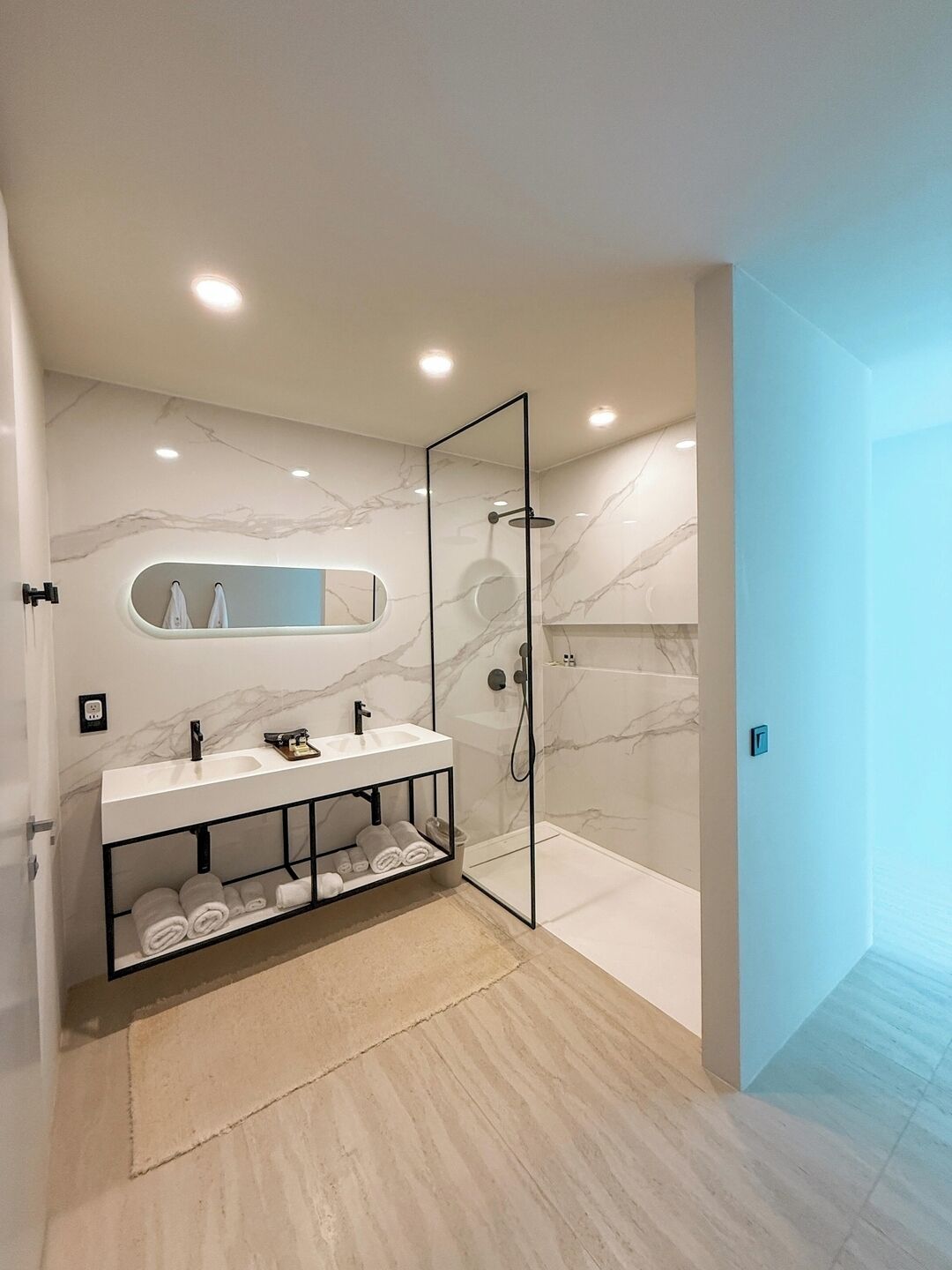 Un baño moderno con ducha envuelta en vidrio, tocador con encimera de mármol y estante empotrado para toallas.