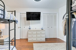 Un dormitorio con literas, cómoda, televisor y armarios blancos.