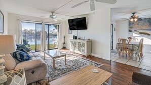 A spacious living room with a large sofa, a coffee table, and a TV mounted on the wall. There is a dining area with a table and chairs, and a ceiling fan. - 3 Mi to Surfside Beach & Pier: Townhome w/ Balcony (Myrtle Beach)