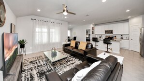 A modern living room with a black leather sofa, a glass coffee table, and a dining area with a white table and chairs. - Rammies Exquisite 4BR in Katy (katy)