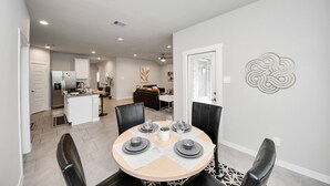A modern dining area with a round table set for four, surrounded by black chairs. A kitchen and living area are visible in the background. - Rammies Exquisite 4BR in Katy (katy)