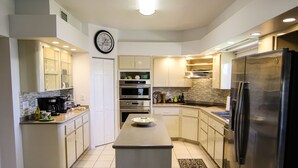Une cuisine moderne avec un îlot central, des appareils en acier inoxydable et une horloge au mur.