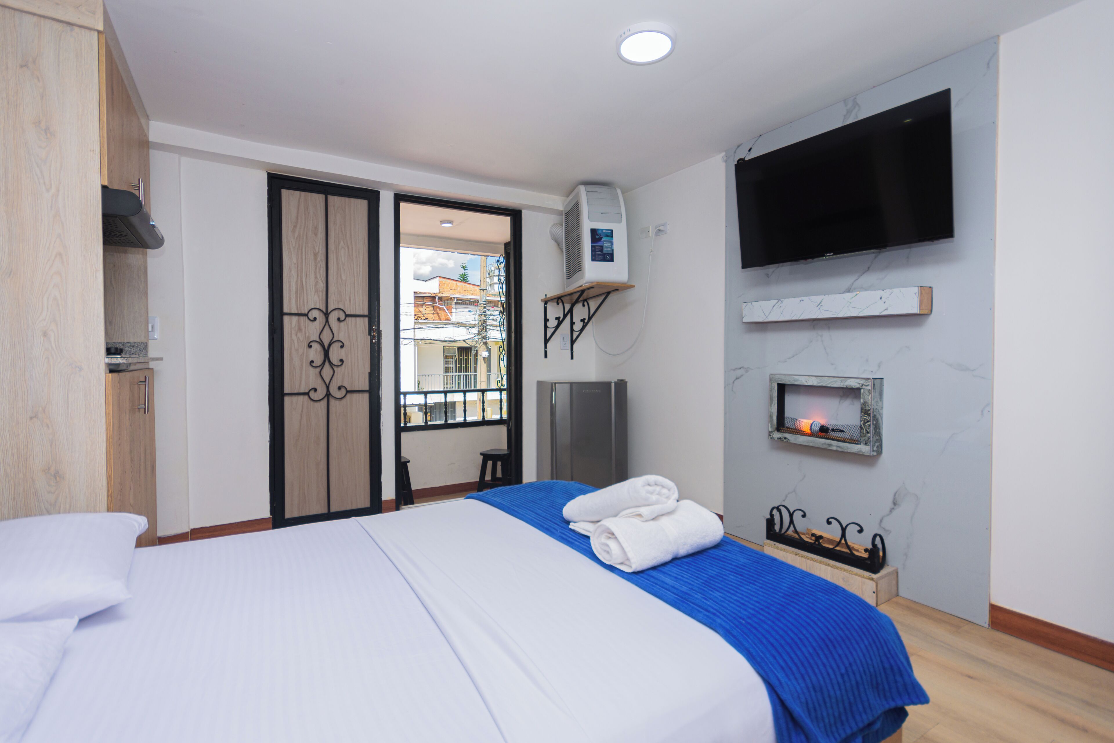 A hotel room with a bed, a TV mounted on the wall, a minibar, and a sliding door leading to a balcony.