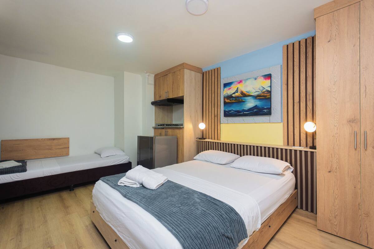Een hotelkamer met twee eenpersoonsbedden, een houten garderobe, een schilderij aan de muur en een kitchenette.