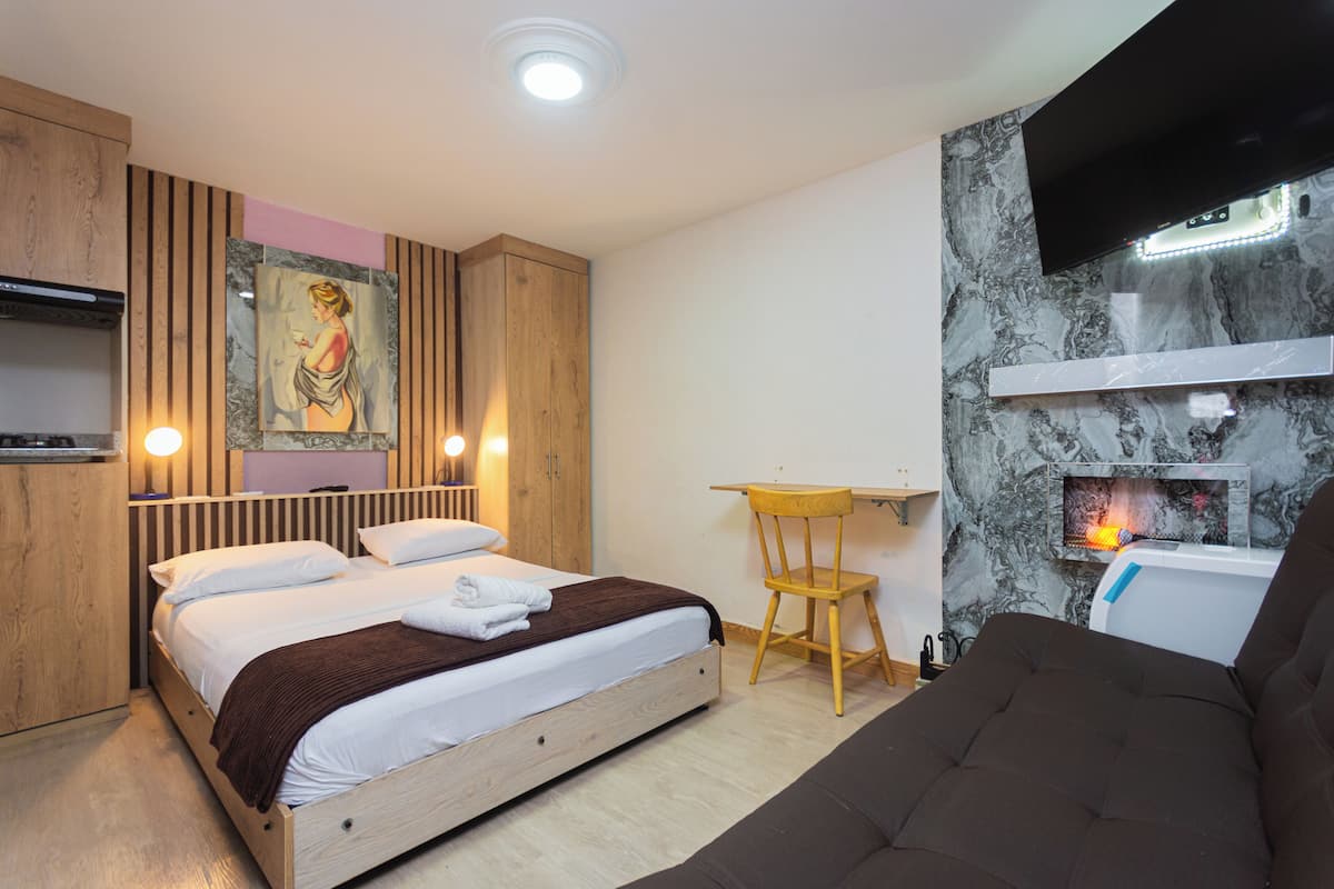 Een moderne slaapkamer met een bed, een houten bureau, een stoel, een aan de muur bevestigde televisie en een open haard.
