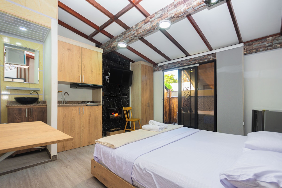 Une chambre compacte comprenant un lit, une table en bois, un petit coin cuisine et une salle de bain dotée d’une porte coulissante.