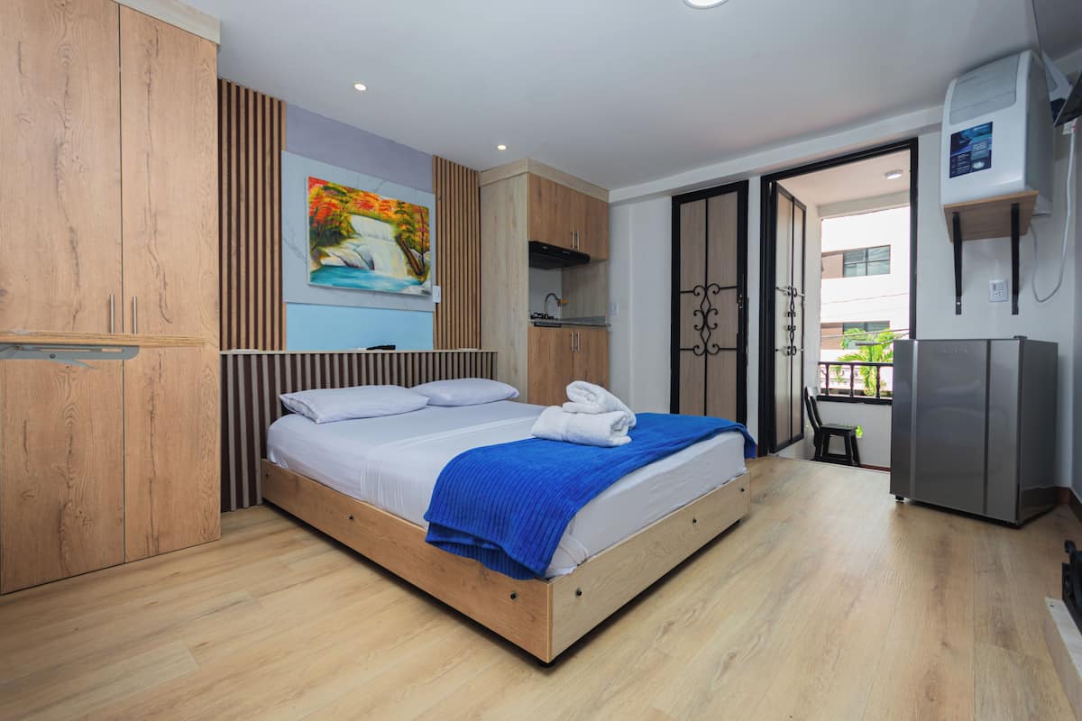 Een slaapkamer met een houten bed, een blauwe deken, een schilderij aan de muur en een balkon met uitzicht.