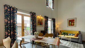 A modern living room with a glass dining table, wooden chairs, a sofa, and patterned curtains.
