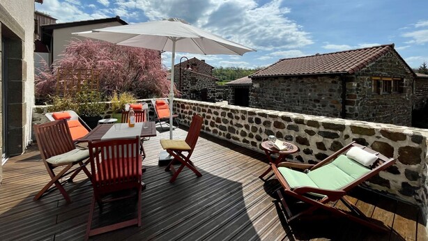 A wooden deck with outdoor furniture, a large umbrella, and stone buildings in the background.