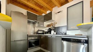 A modern kitchen with stainless steel appliances, wooden ceiling beams, and a white backsplash.