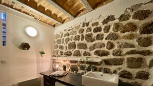 A compact bathroom with a stone wall, a washing machine, a sink, and a small window.