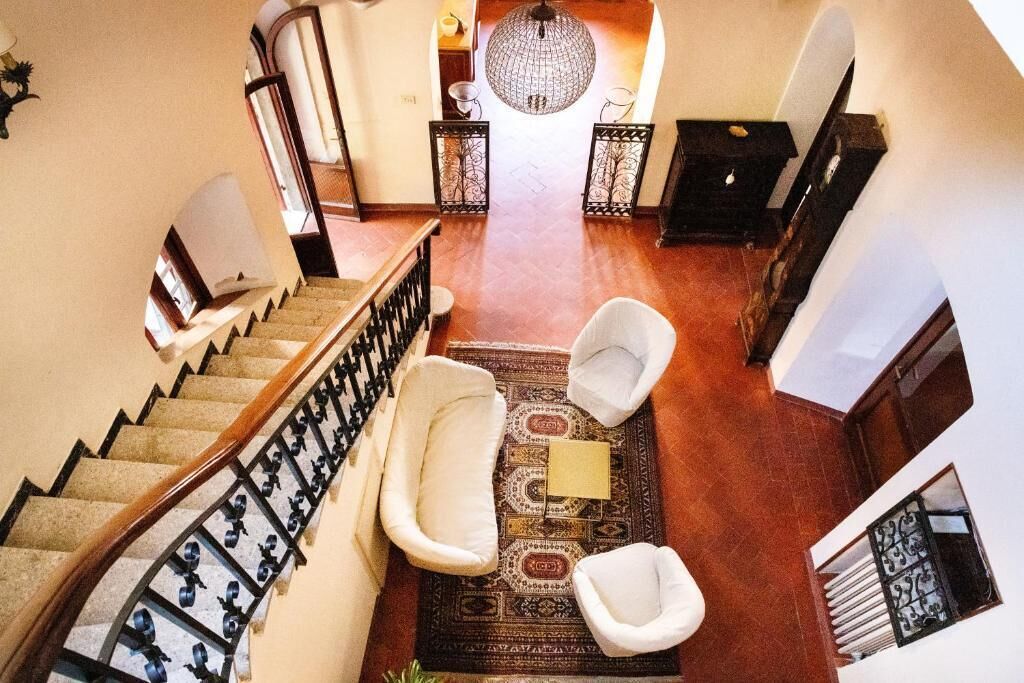 A spacious hallway with a wooden staircase, a large chandelier, and a patterned rug.