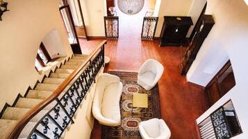 A spacious hallway with a wooden staircase, a large chandelier, and a patterned rug.