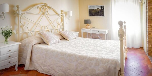 A bedroom with a bed, a nightstand, a lamp, and a painting on the wall. - Hotel Il Castello (Certaldo)