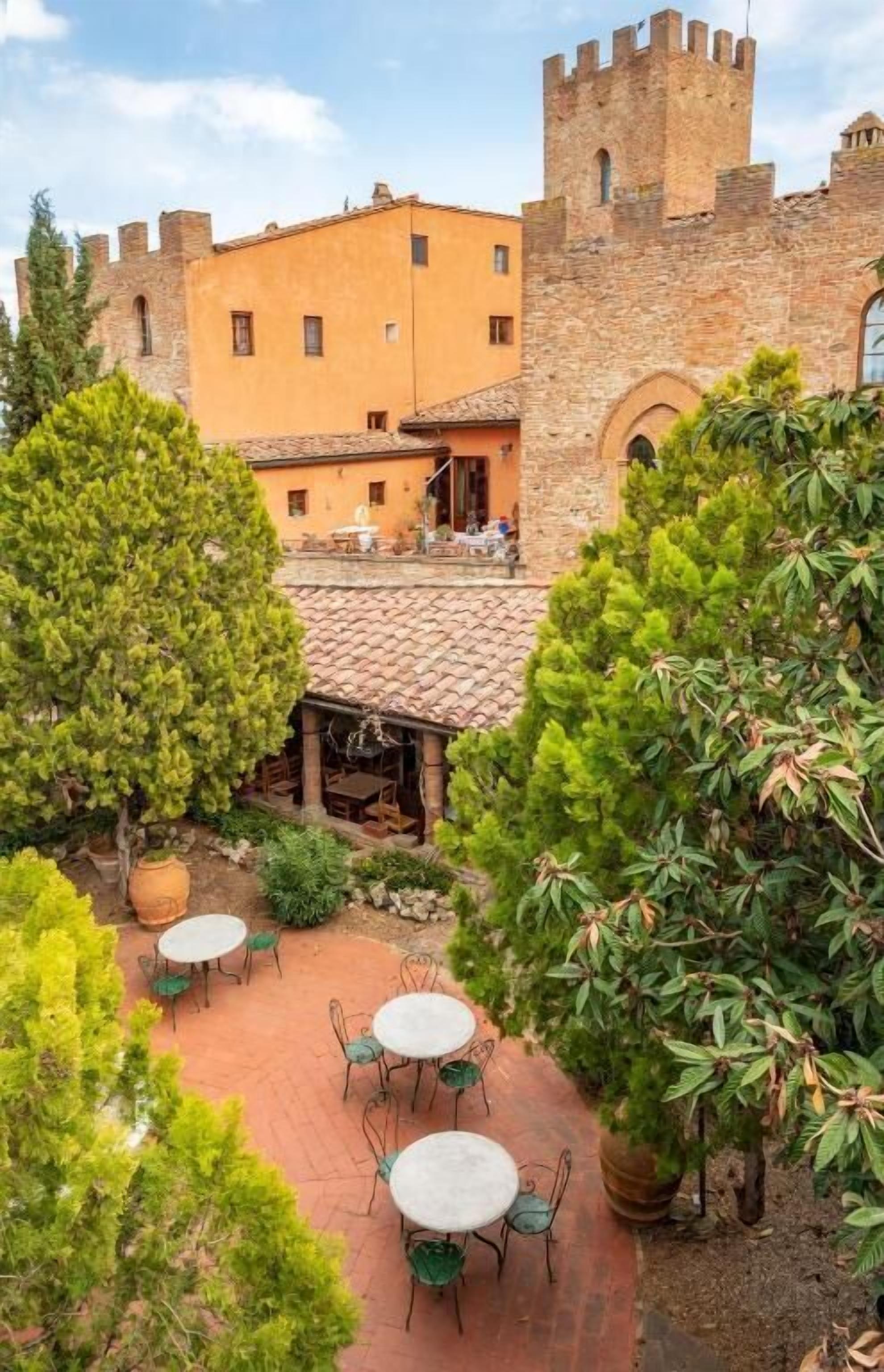 A courtyard with stone walls, a tower, and outdoor seating.