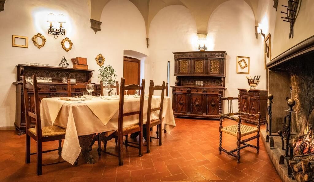 A dining room with a wooden table set for four, surrounded by chairs. There is a fireplace with a mantle and a wooden cabinet to the right.