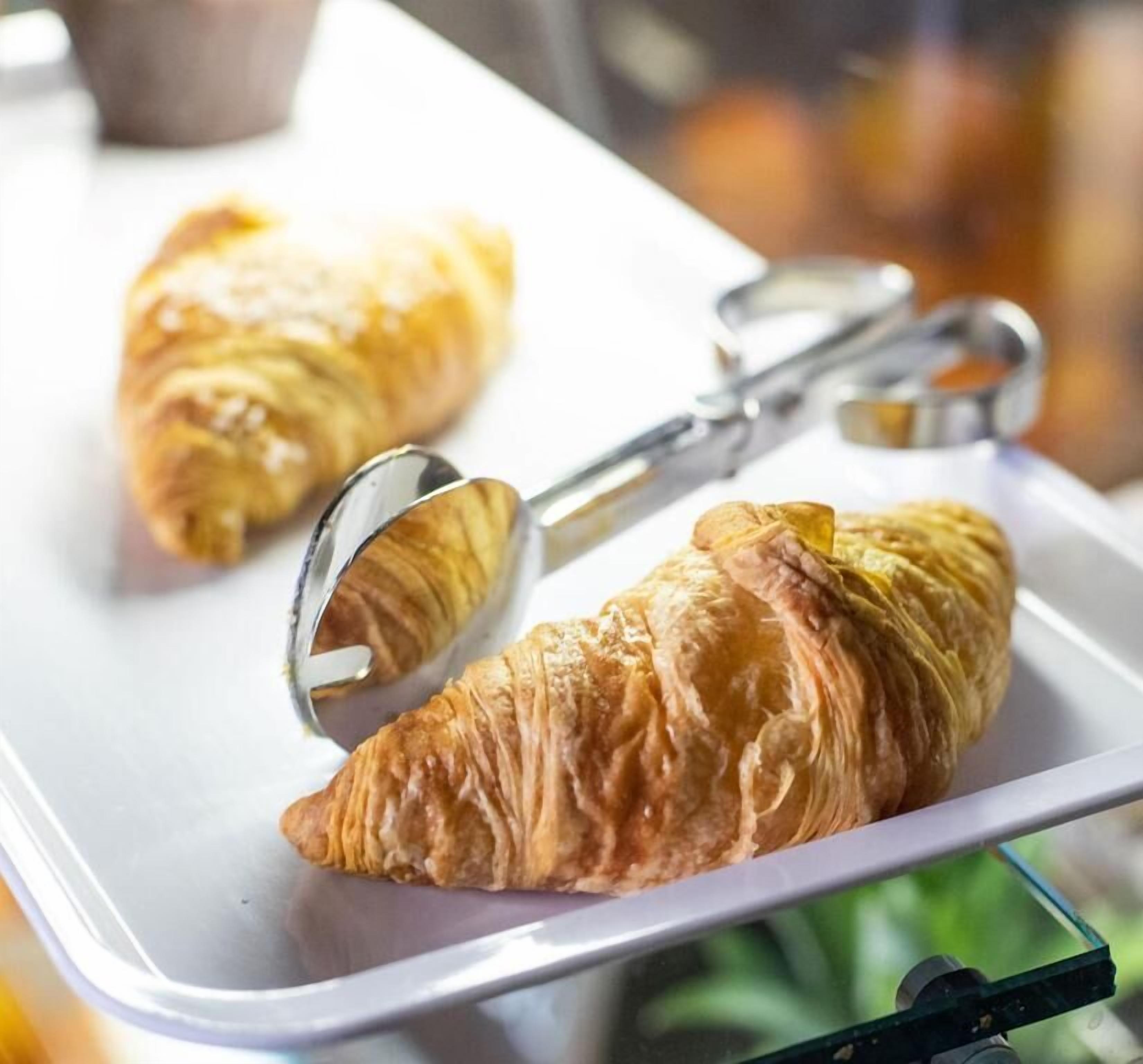 A croissant on a white tray with a metal cutter.