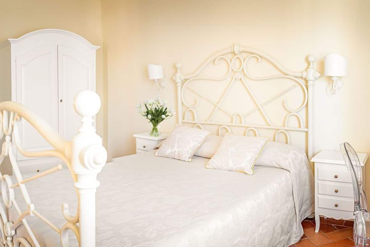 Un dormitorio con una cama blanca, un armario blanco y una mesita de noche con una lámpara.