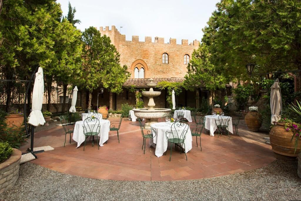 Un patio al aire libre con mesas y sillas, una fuente y un edificio de estilo castillo al fondo.