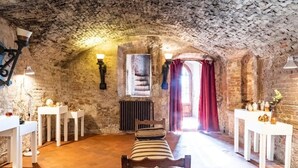 A rustic room with a stone ceiling, a bench, white tables, and a window with red curtains.