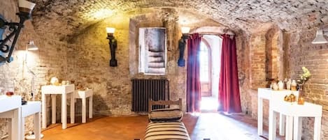 A rustic room with a stone ceiling, a bench, white tables, and a window with red curtains.