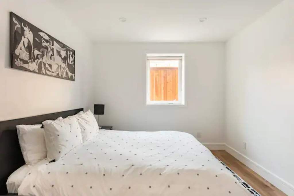 Une chambre à coucher avec un lit, une fenêtre avec des rideaux, un tableau au mur et une table de chevet.