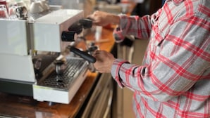 Una persona usando una máquina de café en una cocina con paredes de madera y una ventana.