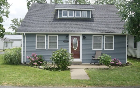 A single-story house with a gray exterior, a red door, and a small porch with a bench.