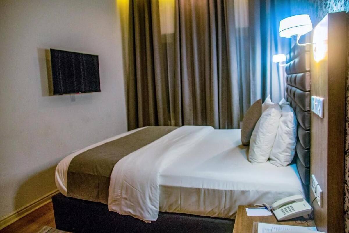 A hotel room with a bed, a bedside telephone, and a flat-screen TV mounted on the wall.