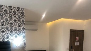 A hotel room with a bed, a sofa, a chair, a bedside table with a phone, and a door with a no-smoking sign. - Crownsville Hotel - Airport Road (Ozuaha)