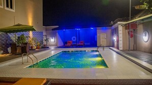 An indoor swimming pool with a tiled floor, a small poolside area with a chair and umbrella, and a blue-lit background. - Crownsville Hotel - Airport Road (Ozuaha)
