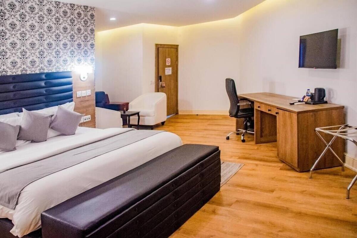 A hotel room with a bed, a desk, a chair, and a television on the wall.