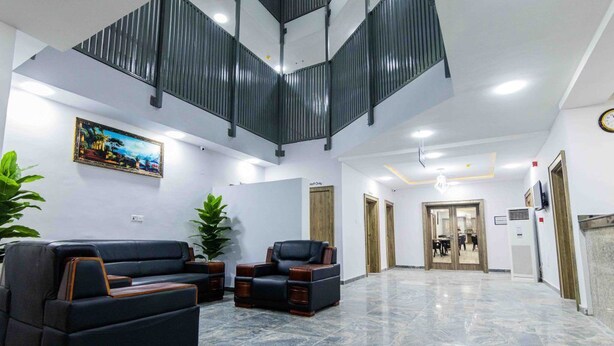 A spacious lobby with a high ceiling, a seating area with sofas, a large potted plant, and a staircase. - Crownsville Hotel - Airport Road (Ozuaha)